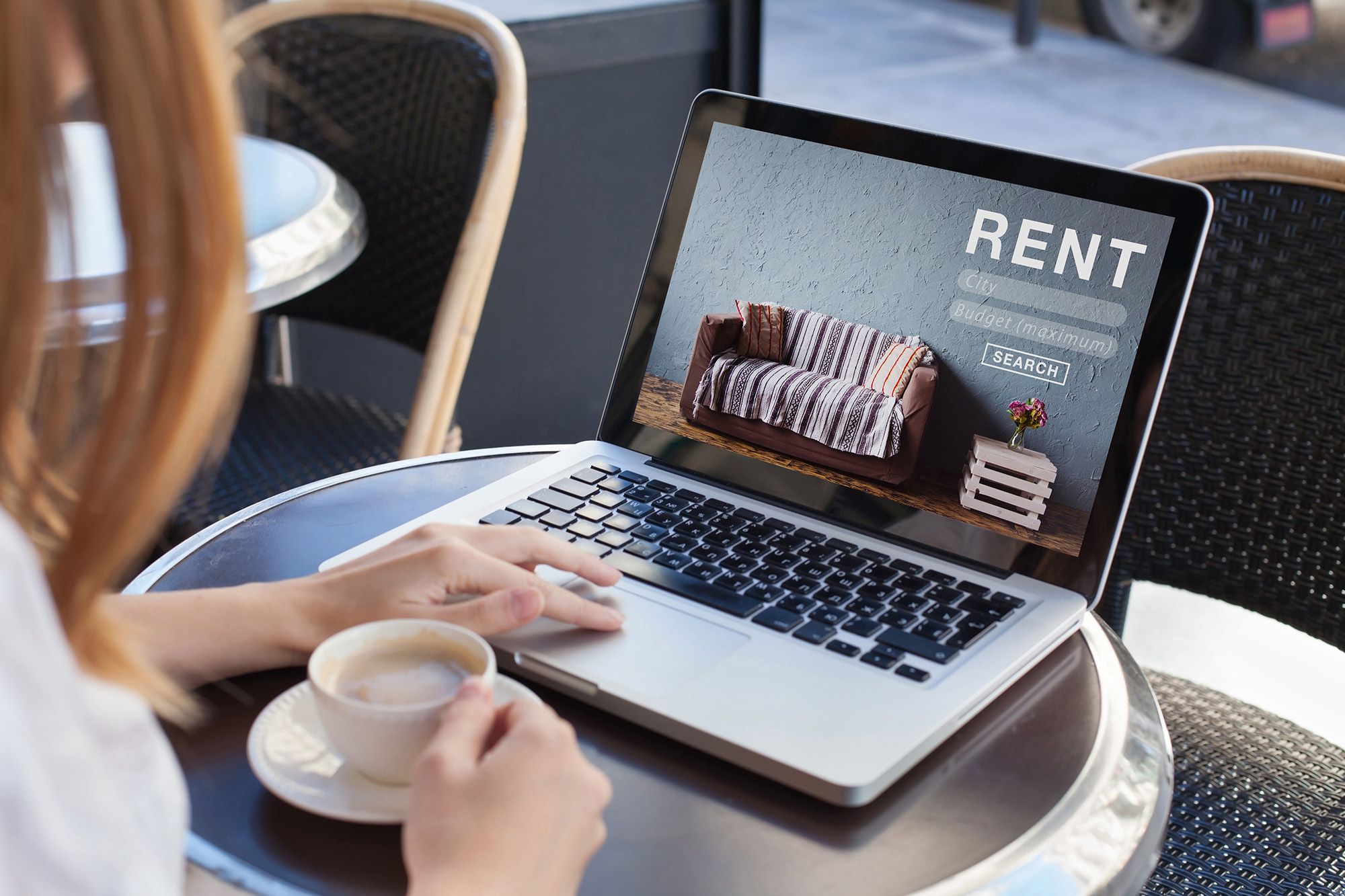 A person sitting at a cafe table, searching for a rental on a laptop